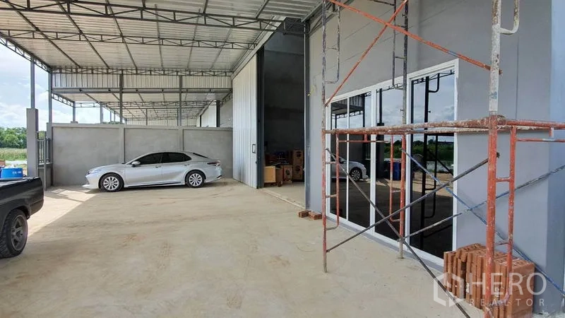 Warehouse for rent in Lam Luk Ka, Pathum Thani - Covered loading and parking area beside glass-front office and tall warehouse entry.
