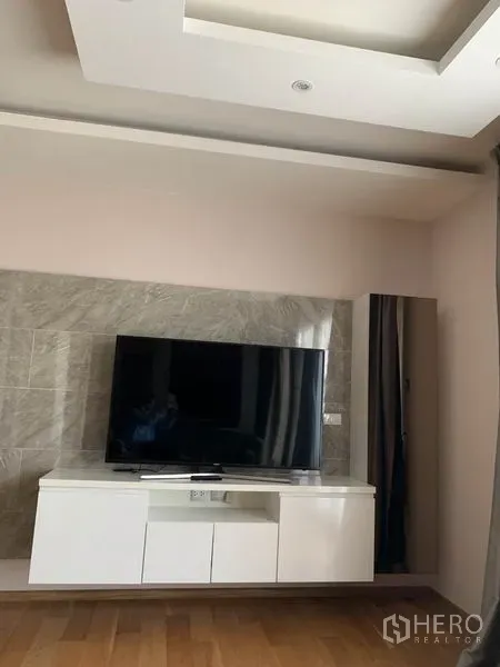 Condominium for rent in Watthana, Bangkok - Living area with flat-screen TV on a white media console and stone accent wall.
