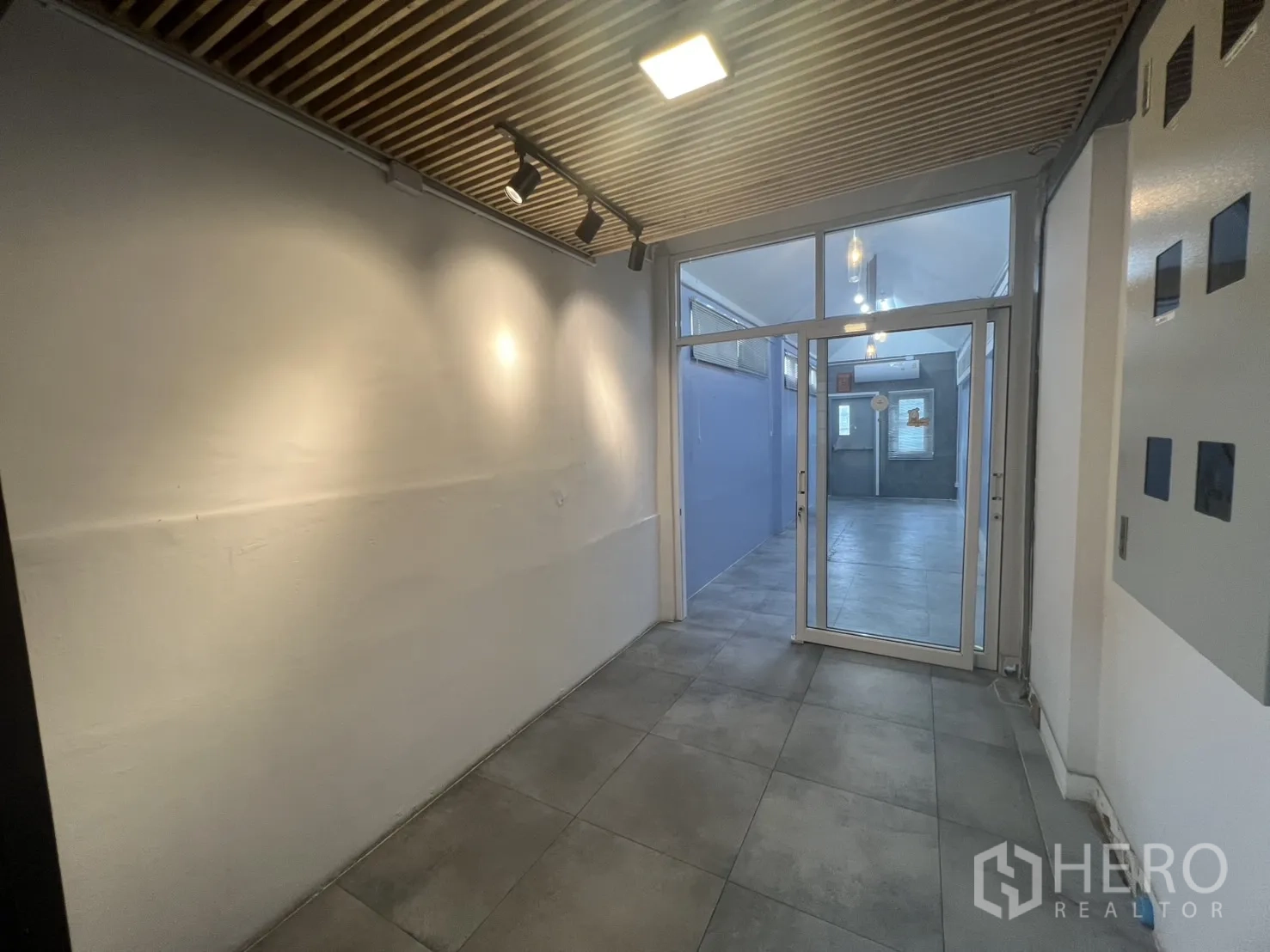 Retail Space for rent - Entrance corridor with wood slat ceiling, spotlights and a glass door leading to a compact retail unit.
