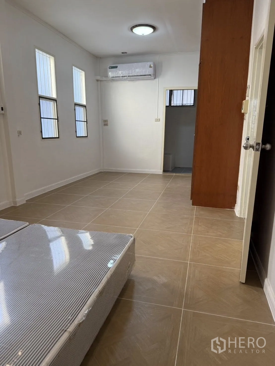 Detached House for rent in Khlong Toei, Bangkok - Bright tiled room with slim windows, air conditioner, and a doorway to a bathroom.