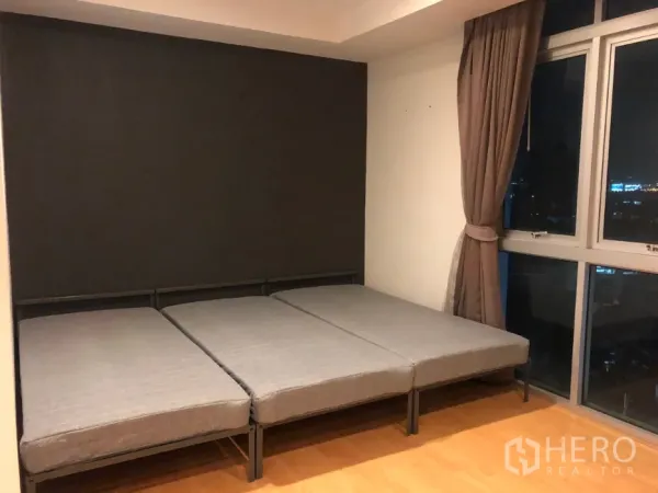Condominium for sale in Khlong Toei, Bangkok - Bedroom with low-profile bed frames beside corner windows with curtains and skyline views.