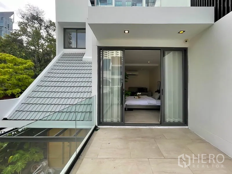 Townhouse for rent in Khlong Toei, Bangkok - Spacious terrace with glass railing and sliding doors to a bedroom.