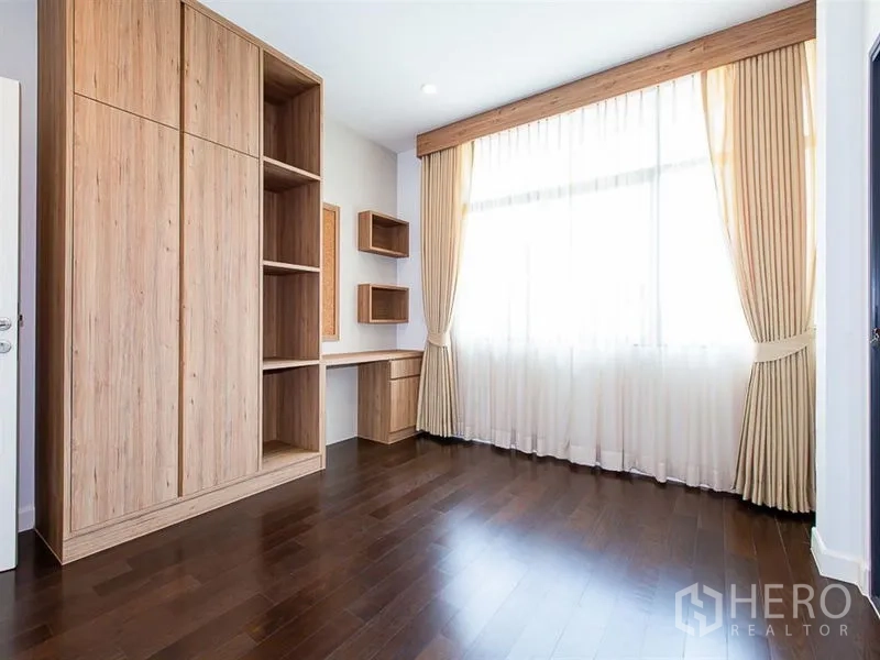 Detached House for rent or sale in Prawet, Bangkok - Bedroom with built-in wardrobe, work desk and a large curtained window.