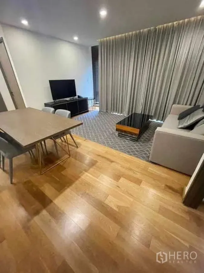 Condominium for rent or sale in Khlong Toei, Bangkok - Alternate view of the living zone with dining table, sofa, TV unit and long curtains.