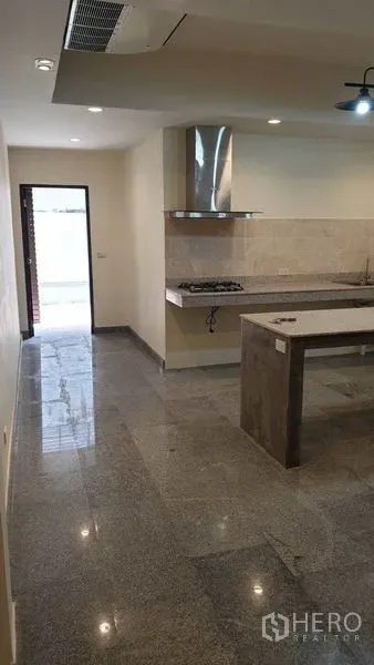 Townhouse for rent or sale in Khlong Toei, Bangkok - Modern kitchen with island, gas hob and hood opening to a rear patio area.