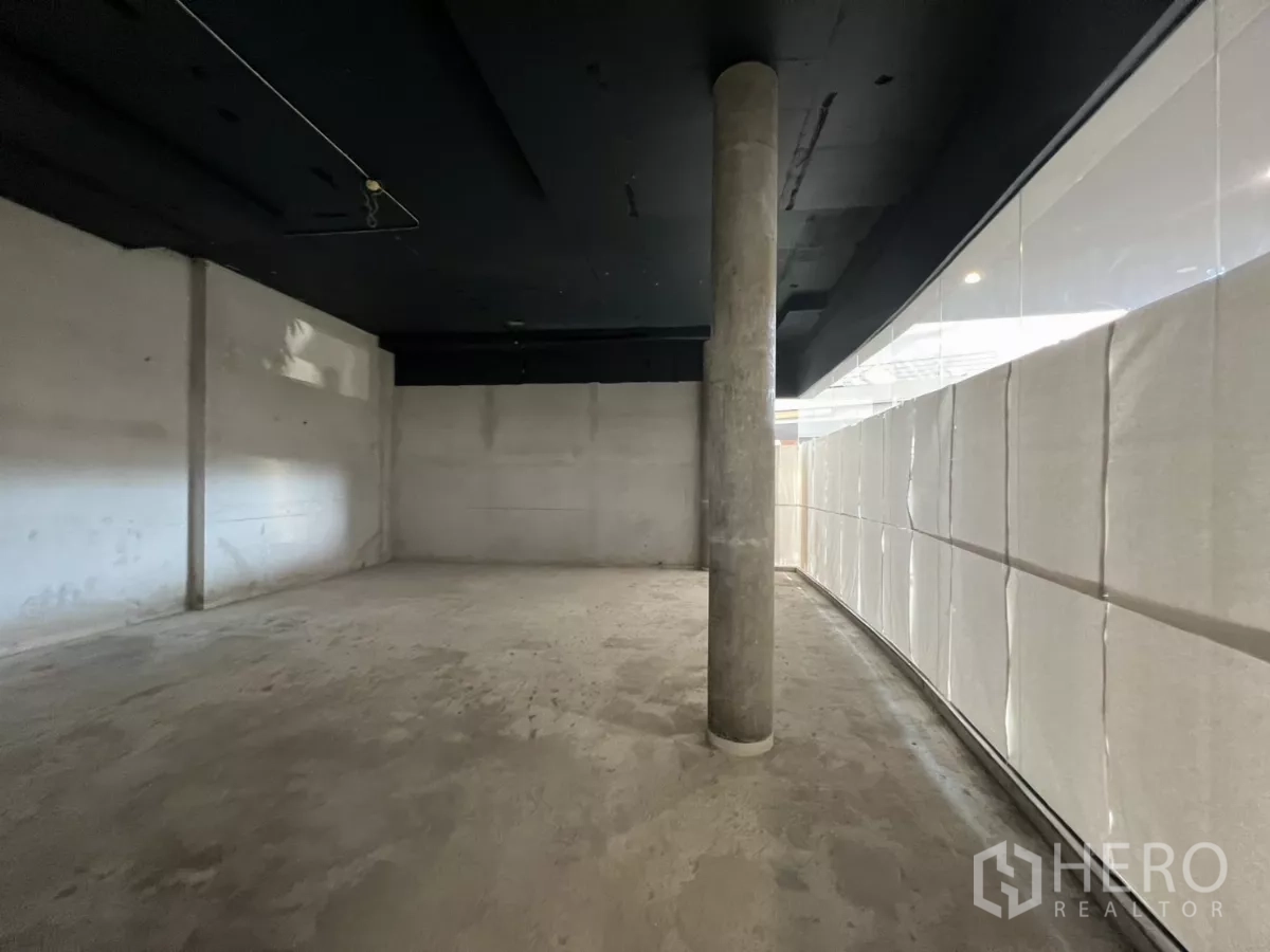 Retail Space for rent - Unfurnished shop interior with high ceiling, concrete surfaces and a column beside the window wall.