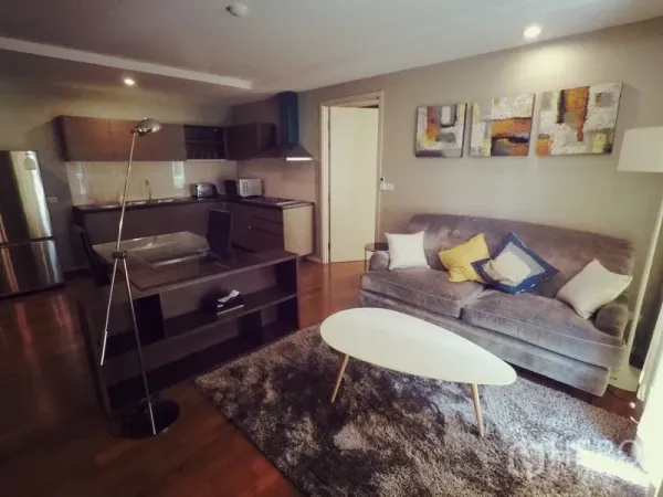 Condominium for rent or sale in Khlong Toei, Bangkok - Cozy living room with gray sofa, shag rug, modern artwork and an open kitchen in the background.