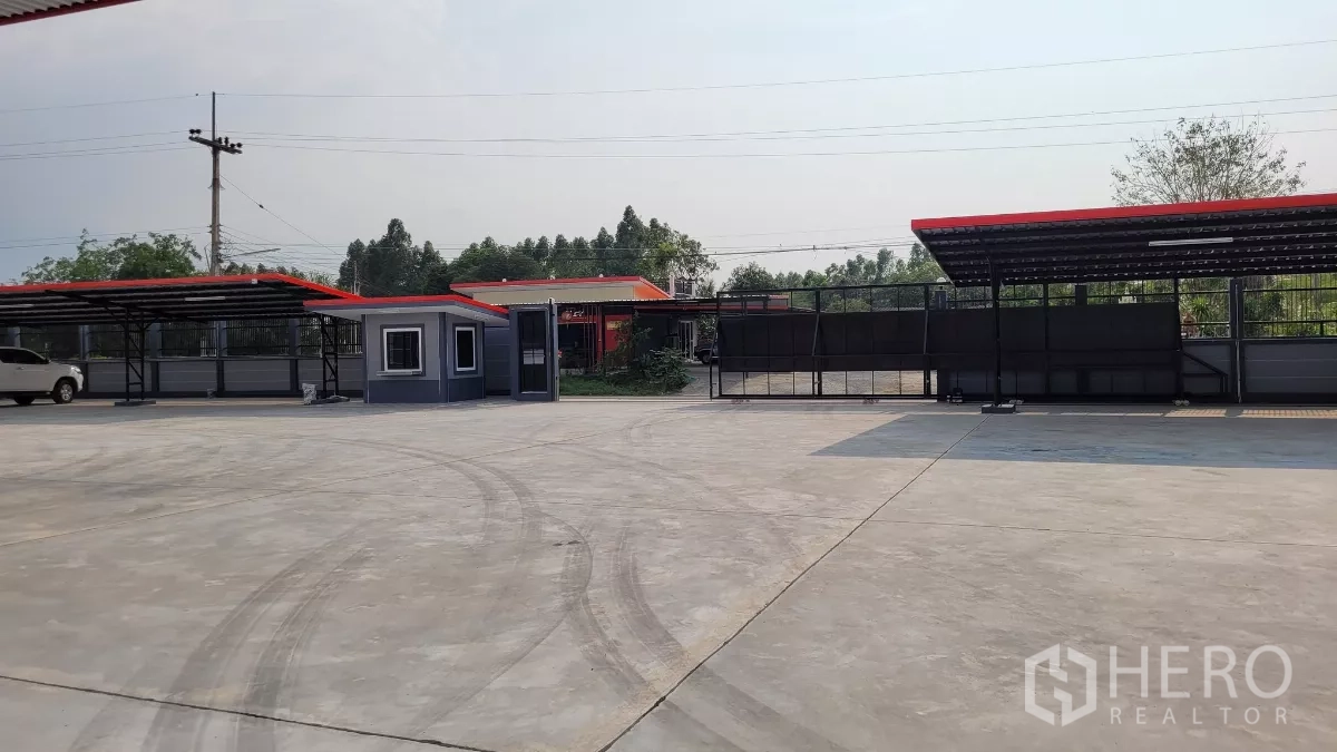 Factory for rent or sale in Phanat Nikhom, Chon Buri - Wide concrete yard with covered parking, guard booth and sliding gate.
