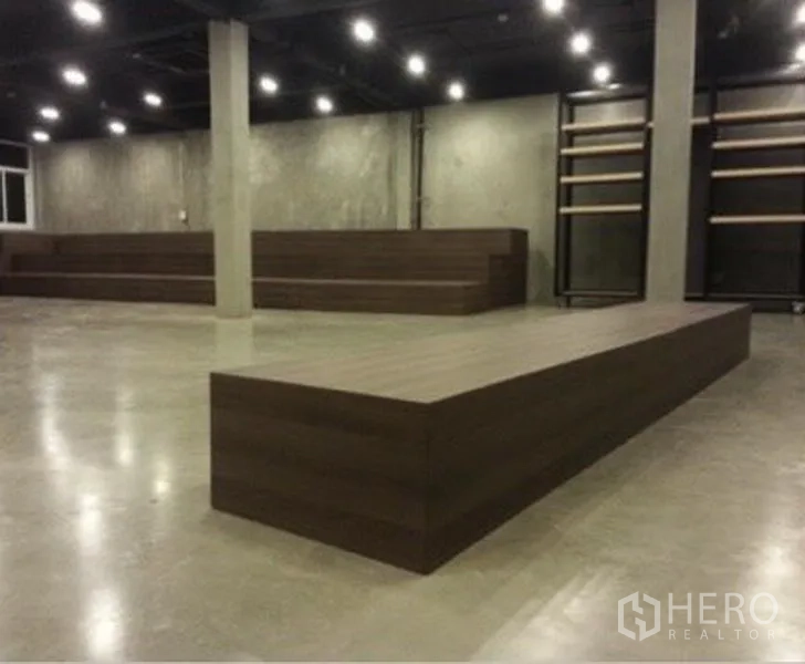 Shophouse for rent in Suan Luang, Bangkok - Spacious open-plan showroom with polished concrete floors, dark ceiling with spotlights, wooden display platforms, and shelving.