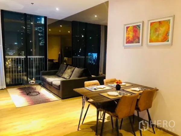 Condominium for rent in Khlong Toei, Bangkok - Open-plan living and dining area with wood floors, sofa, dining set and floor-to-ceiling windows overlooking the Bangkok skyline at night.