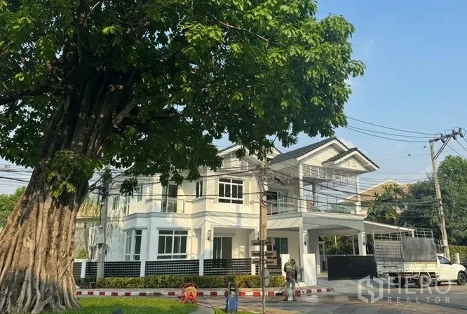 บ้าน ขายในPak Kret, Nonthaburi - ด้านหน้าบ้านใต้ร่มไม้ใหญ่ เห็นระเบียง ประตูรั้ว และที่จอดรถในร่ม