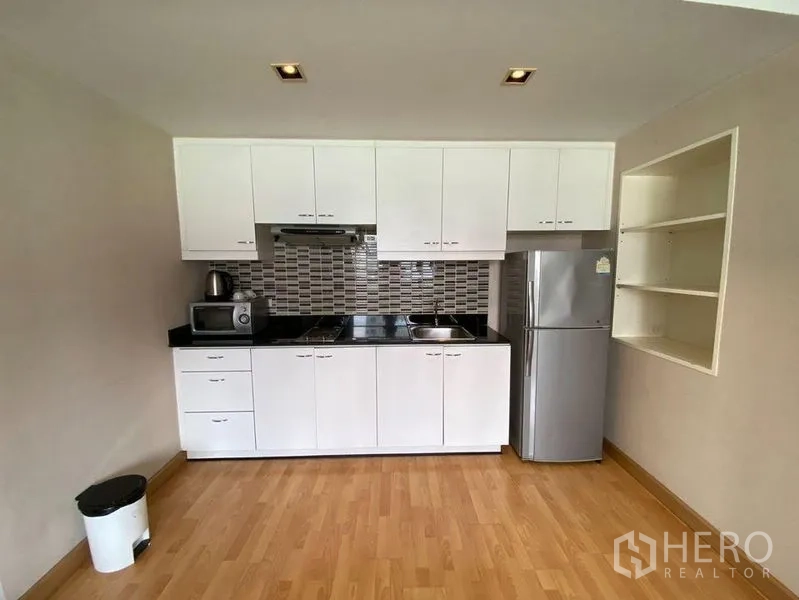 Condominium for rent in Khlong Toei, Bangkok - Compact white kitchen with mosaic backsplash, granite countertops, and a full-size fridge.