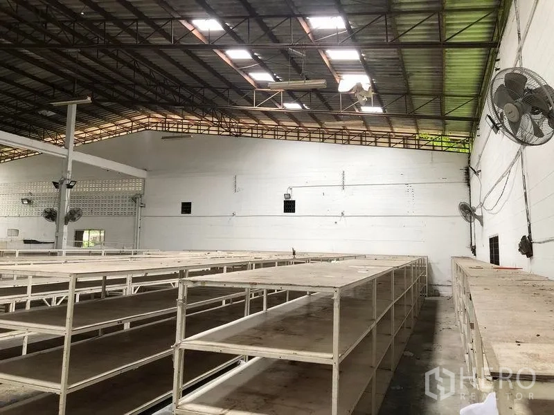 Warehouse for rent in Bang Kapi, Bangkok - Rows of heavy-duty shelves beneath high roof with wall-mounted industrial fans.
