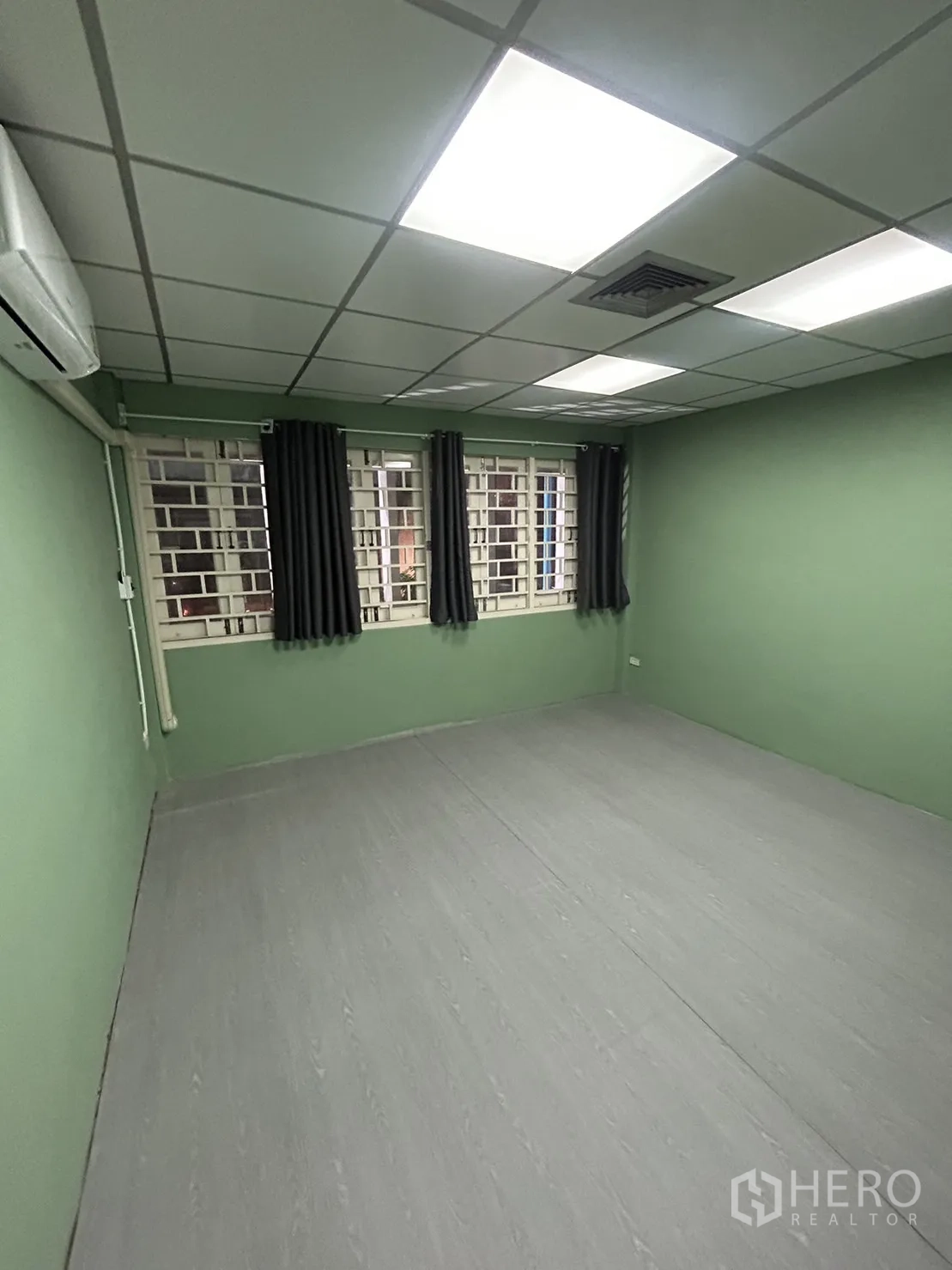 Shophouse for rent in Khlong Toei, Bangkok - Green office room with ceiling panel lights, barred windows, and curtains.