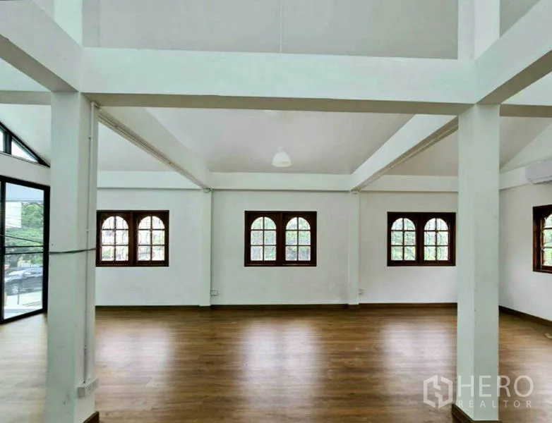 Home Office for rent in Lat Phrao, Bangkok - Large open-plan room with multiple arched windows and warm wood flooring.