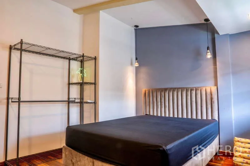 Townhouse for rent in Khlong Toei, Bangkok - Bedroom with upholstered headboard, pendant lights and an open metal rack.