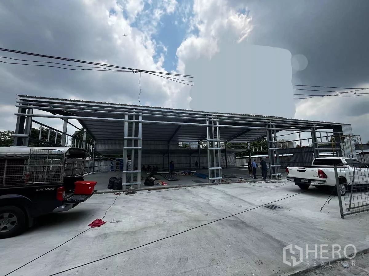 Warehouse for rent in Lak Si, Bangkok - Front exterior of the warehouse under construction with a wide concrete yard and pickup truck access.