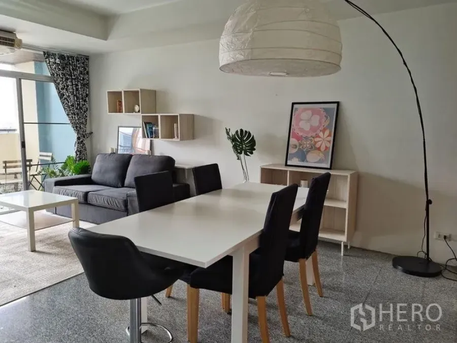 Condominium for rent in Khlong Toei, Bangkok - Open-plan living and dining area with table for four and floor lamp beside the balcony.