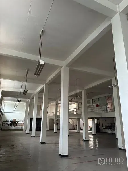 Shophouse for rent in Khlong Toei, Bangkok - Open-plan hall with white pillars, suspended lights and a mezzanine office area inside a Bangkok shophouse.