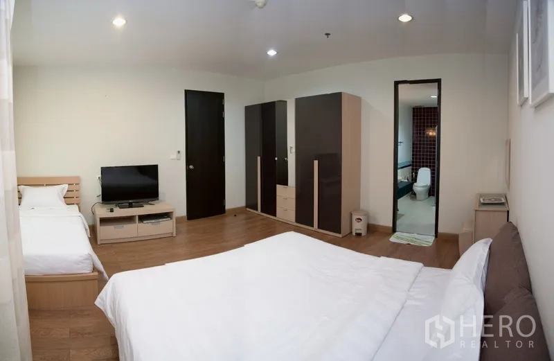 Condominium for rent in Khlong Toei, Bangkok - Master bedroom view with wardrobes, TV stand and entrance to an ensuite bathroom.