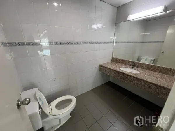 Office Space for rent or sale - Clean tiled restroom with toilet, large wall mirror and granite countertop sink.