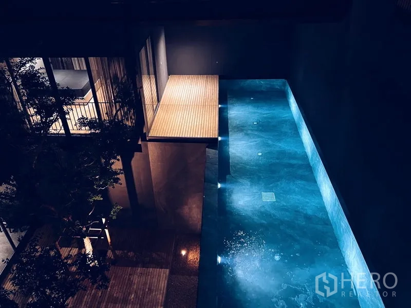 Detached House for rent or sale in Bangkok - Night view of illuminated private lap pool with wooden deck.