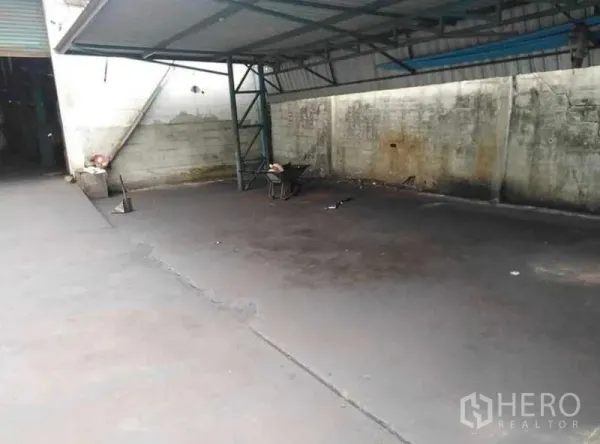 Warehouse for rent in Prawet, Bangkok - Covered loading bay with metal canopy and spacious concrete yard for trucks.