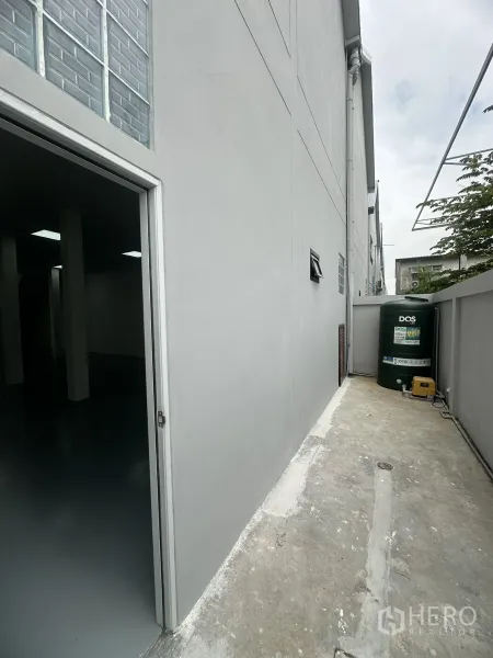 Warehouse for sale in Khlong Luang, Pathum Thani - Side service yard with external door and water system tank beside the warehouse.