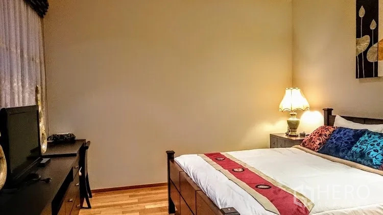 Condominium for rent in Khlong Toei, Bangkok - Bedroom corner with wood flooring, desk and TV console next to curtained window.