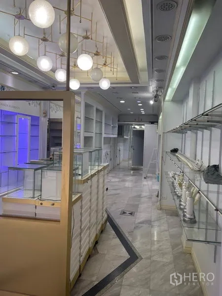 Shophouse for rent in Bang Rak, Bangkok - Aisle with glass display counters and illuminated shelving leading to the rear.