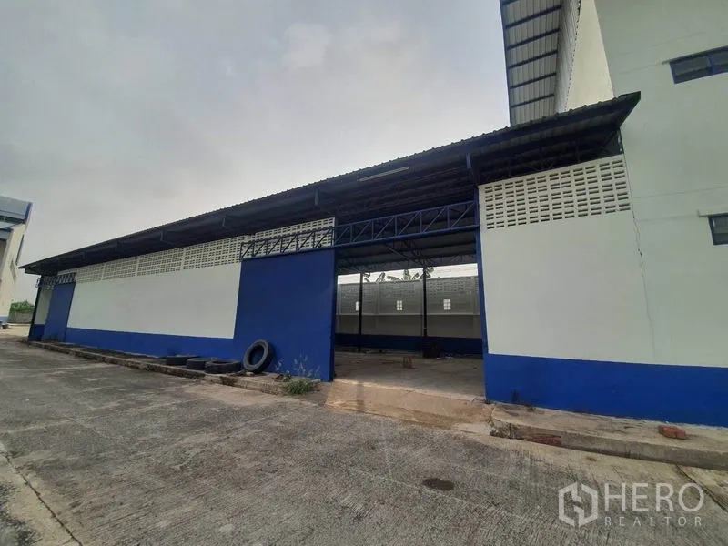 Factory for rent in Bang Bua Thong, Nonthaburi - Side view of a blue-and-white warehouse with a covered loading bay and large doorway.