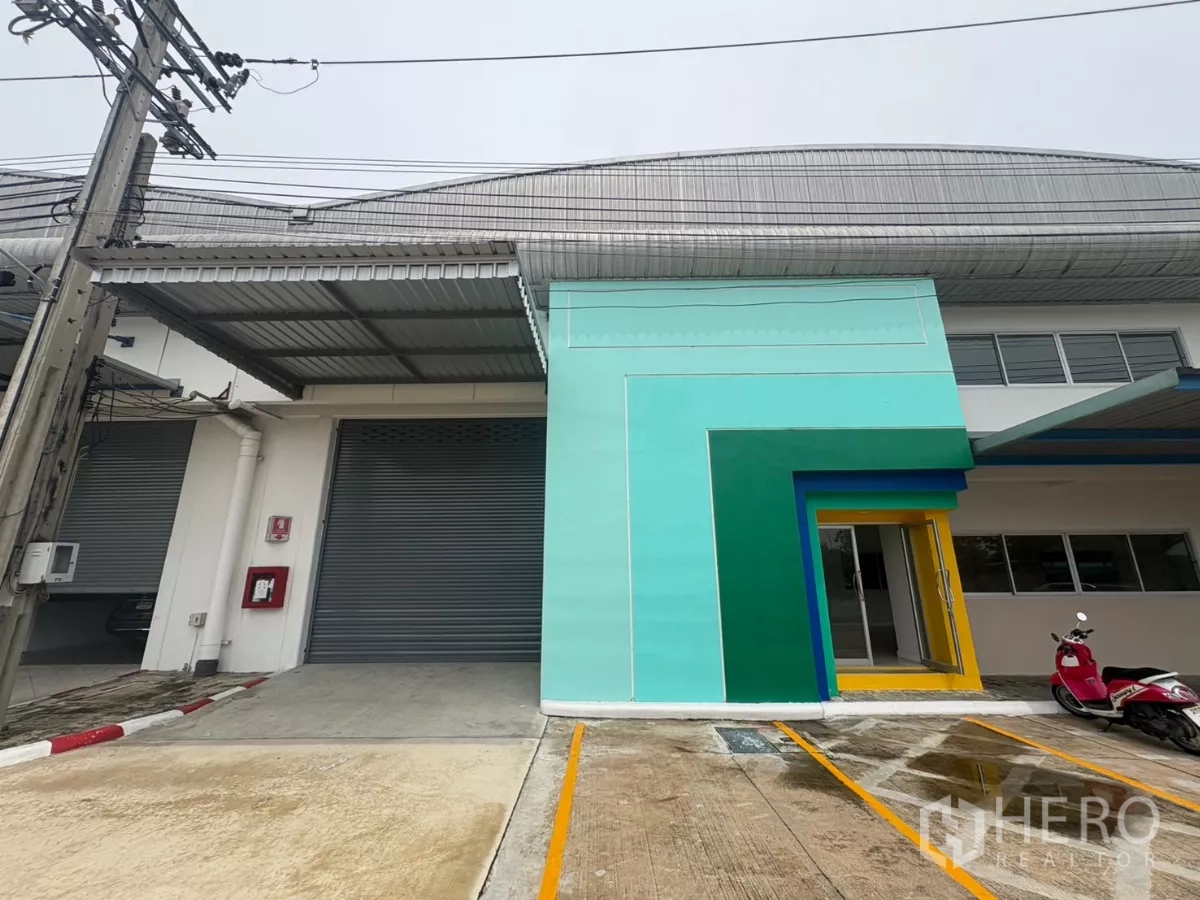 Factory for rent in Bang Phli, Samut Prakan - Loading bay with roller shutter door and colorful office entrance canopy.