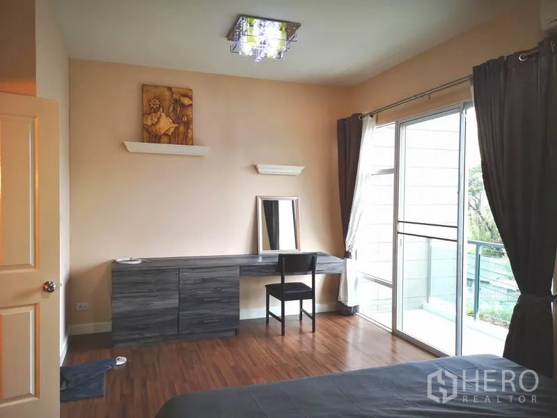 Townhouse for rent in Suan Luang, Bangkok - Master bedroom with long built-in desk, wood floors and sliding doors to balcony.