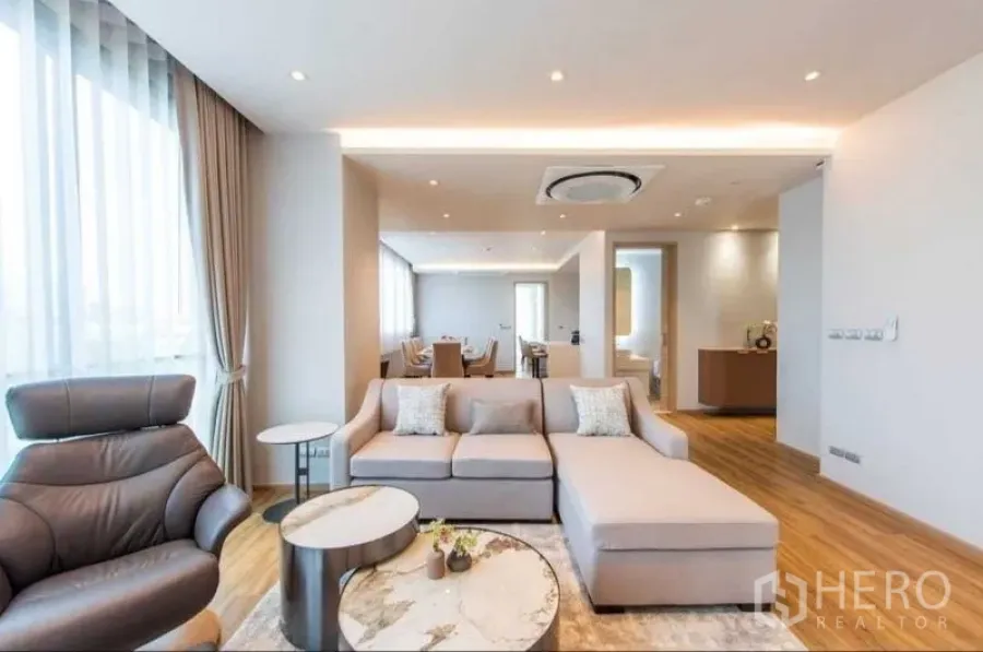 Condominium for rent in Bang Na, Bangkok - Modern open-plan living room with L-shaped sofa, floor-to-ceiling windows and wood floors in a Bang Na condo.