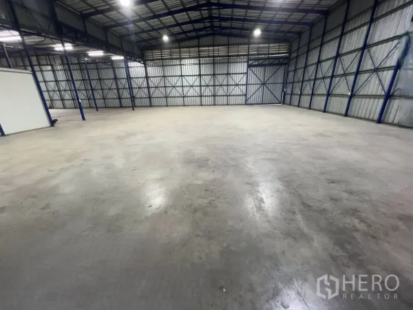 Warehouse for rent in Khlong Luang, Pathum Thani - Open storage area of the warehouse showing steel columns, metal cladding walls, and a smooth concrete surface.