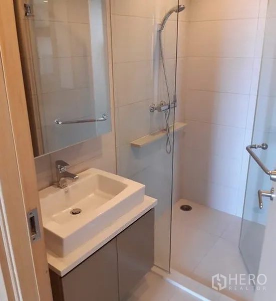 Condominium for rent in Khlong Toei, Bangkok - Compact bathroom with square basin, mirror cabinet, and glass-enclosed shower.
