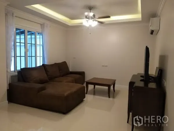 Townhouse for rent in Mueang Samut Prakan, Samut Prakan - Cozy living room with L‑shaped sofa, ceiling fan, and TV cabinet under recessed lighting.