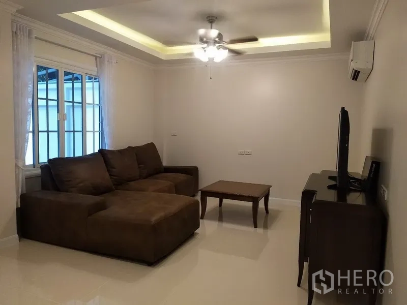 Townhouse for rent in Mueang Samut Prakan, Samut Prakan - Cozy living room with L‑shaped sofa, ceiling fan, and TV cabinet under recessed lighting.