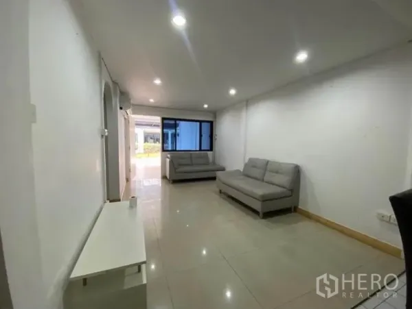 Townhouse for rent in Khlong Toei, Bangkok - Open-plan living room with gray sofas, window, and glossy tile flooring under downlights.