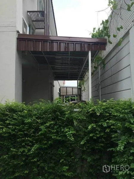 Townhouse for sale in Suan Luang, Bangkok - Side yard with metal awning and privacy wall covered by green vines.