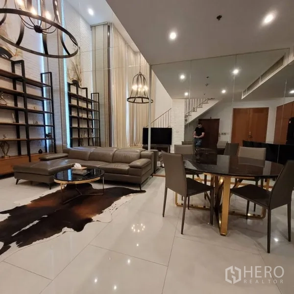 Condominium for rent in Khlong Toei, Bangkok - Open-plan living and dining area with mirrored wall, tall shelving, and pendant lighting.