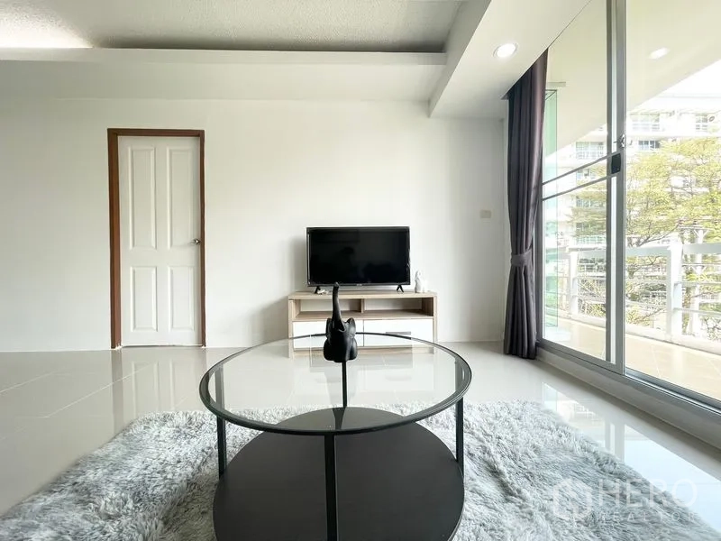 Condominium for rent in Khlong Toei, Bangkok - Living area with TV console and round coffee table near sliding doors.