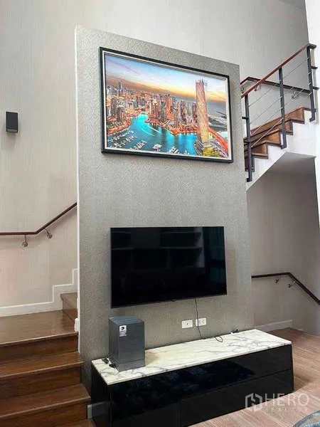 Townhouse for rent in Khlong Toei, Bangkok - TV feature wall with mounted screen, console, and staircase with wooden steps and glass balustrade.