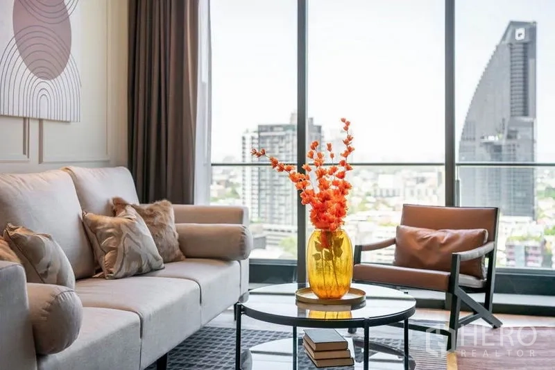 Condominium for rent in Khlong Toei, Bangkok - Sofa and chair by panoramic windows overlooking the Bangkok cityscape.