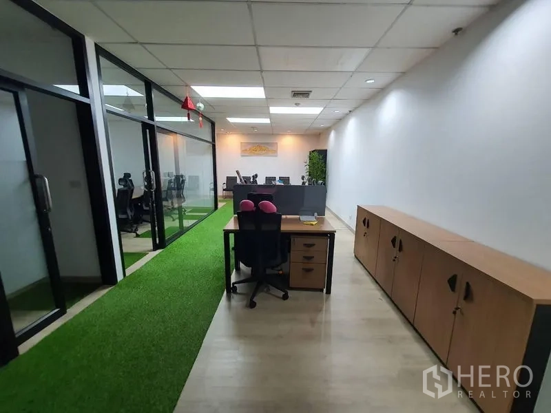 Office Space for rent - Office corridor with glass partitions, storage cabinets, a workstation and a green turf strip.