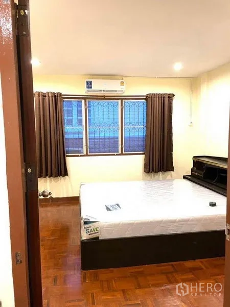 Townhouse for rent in Bang Na, Bangkok - Bright bedroom with parquet flooring, double bed, AC unit and window with security grilles.