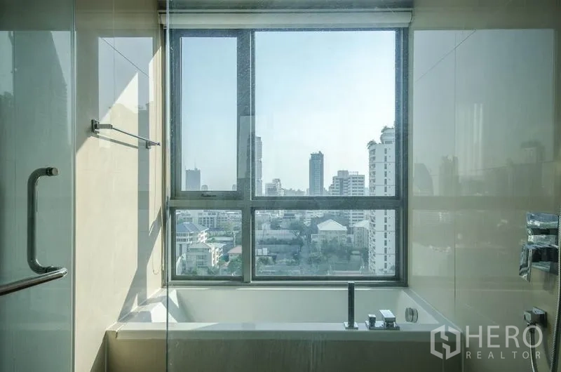 Condominium for rent or sale in Watthana, Bangkok - Bathroom with bathtub and a large window overlooking the Bangkok skyline.