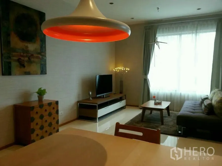 Condominium for rent or sale in Khlong Toei, Bangkok - Bright living room with large window, gray sofa, TV unit and bold pendant light.