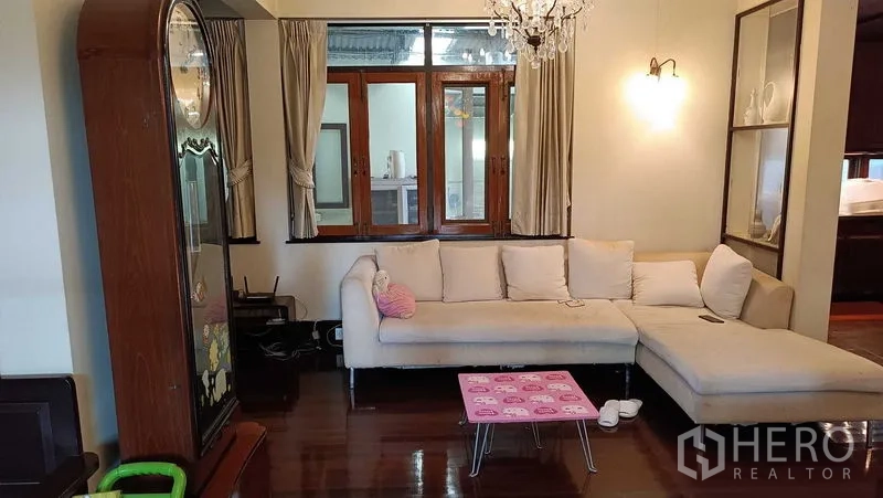Detached House for rent in Phaya Thai, Bangkok - Cozy living room with L-shaped sofa, chandelier, wooden windows and glossy timber floor.