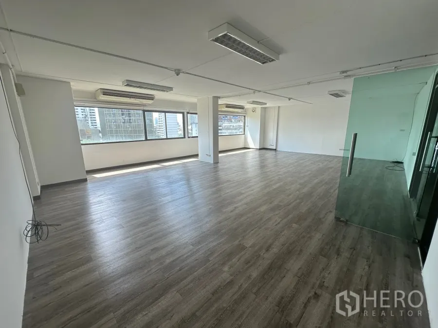 Office Space for rent - Corner view of empty office with glass door partition, dark wood-look floors and abundant natural light.